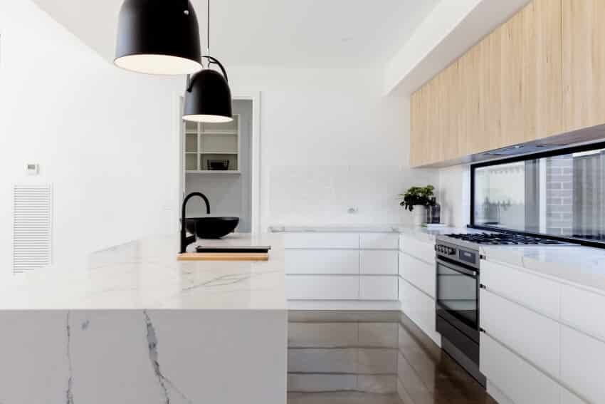 A beautiful white interior kitchen with wooden cabinets, calacatta michelangelo marble countertops, and black fixtures