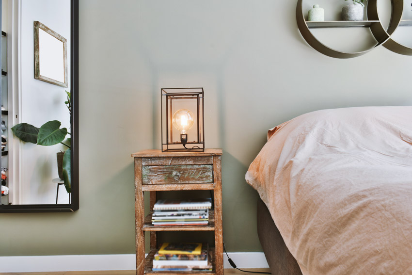 Bedroom with a nightstand, lamp, books, mirror, and comforter