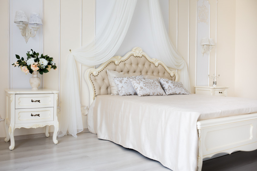 Baroque bedroom with antique white nightstand, headboard, pillows, and wall mounted lamps