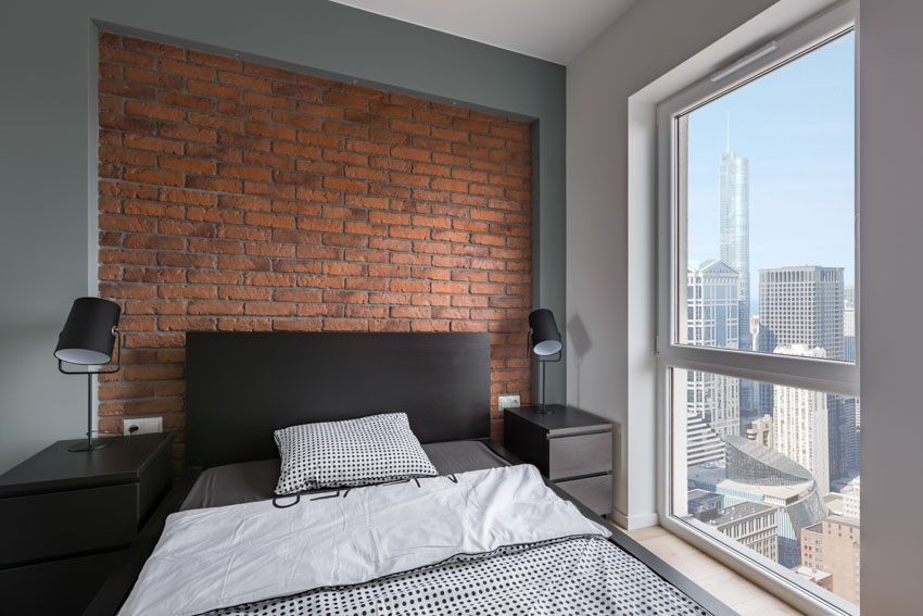 Industrial bedroom with black headboard, brick accent wall, nightstands, lamps, and window