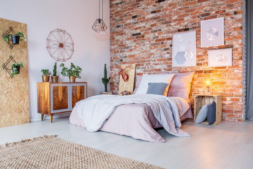 Bedroom with brick accent wall, wood nightstand, floor rug, dresser, and indoor plants