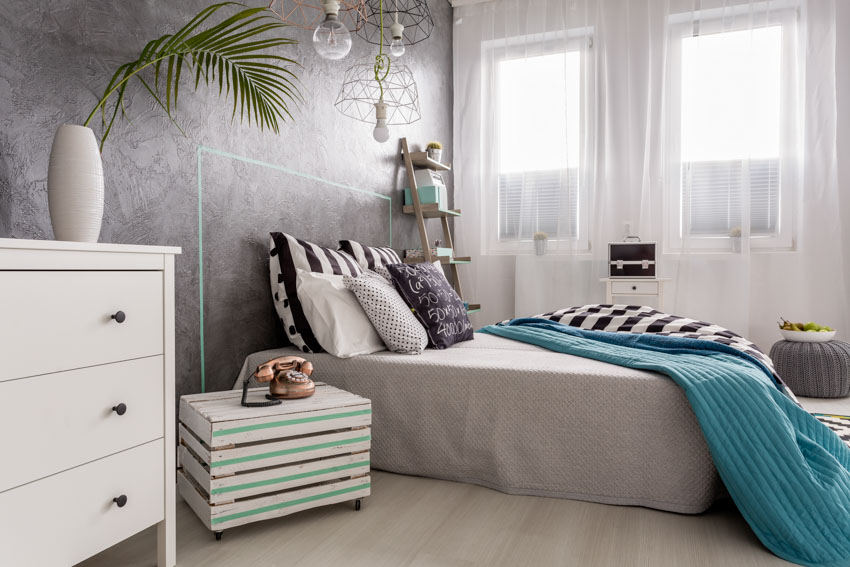 Bedroom with colorful low profile nightstand, white dresser, indoor plant, and sheer curtain