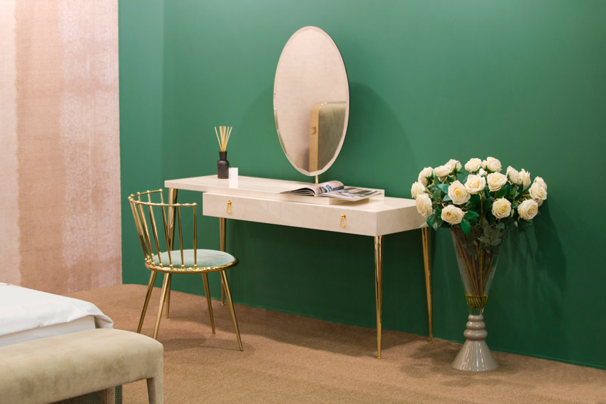 Bedroom with dresser, table, accent chair, mirror, decorative vase, flowers, wood floor, and green wall