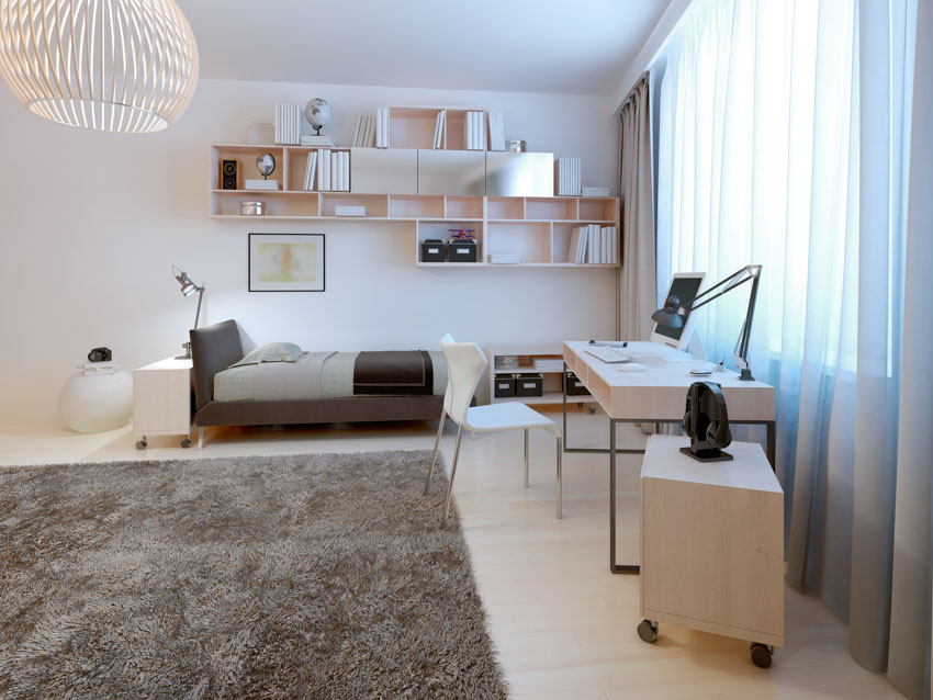 Bedroom with floor rug, portable cart, nightstand, study area, table lamp, chair, floating shelves, and window curtains