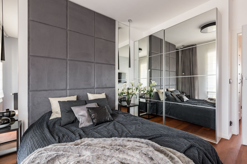 Bedroom with floor to ceiling headboard, pillows, wood flooring, comforter, and custom mirror wall panel