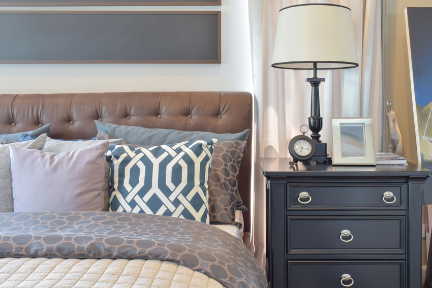 Traditional bedroom with lamp, black nightstand, headboard, pillows, and comforter
