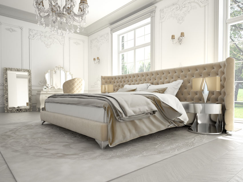 Bedroom with tufted headboard, silver nightstand, carpet, white walls, mirror, windows, and chandelier