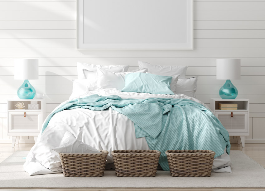 Coastal style bedroom with white siding wall, nightstands, lamps, baskets, pillows, and bedsheets