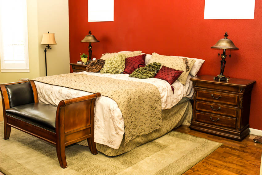 Bedroom witih cushioned seating, distressed nightstand, lamp, red wall, carpet, wood floor, and window
