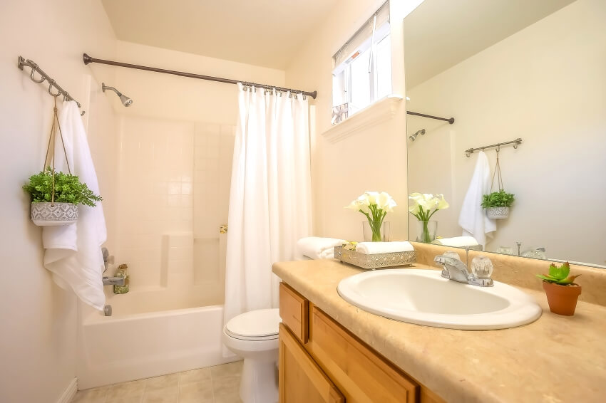 Beige bathroom interior with plants, vanity, and shower bathtub with shower curtain in a rod