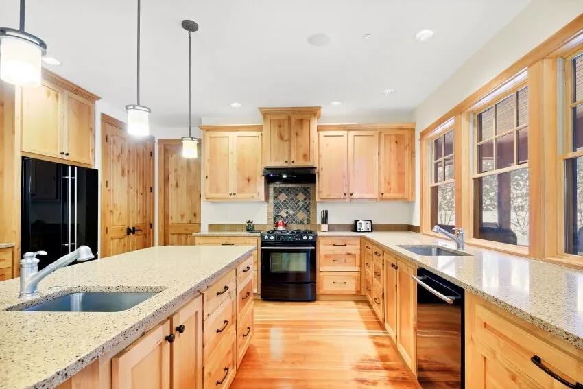 Big kitchen with wooden interior features granite countertops, pendant lights above island, knotty pine cabinets and black appliances 
