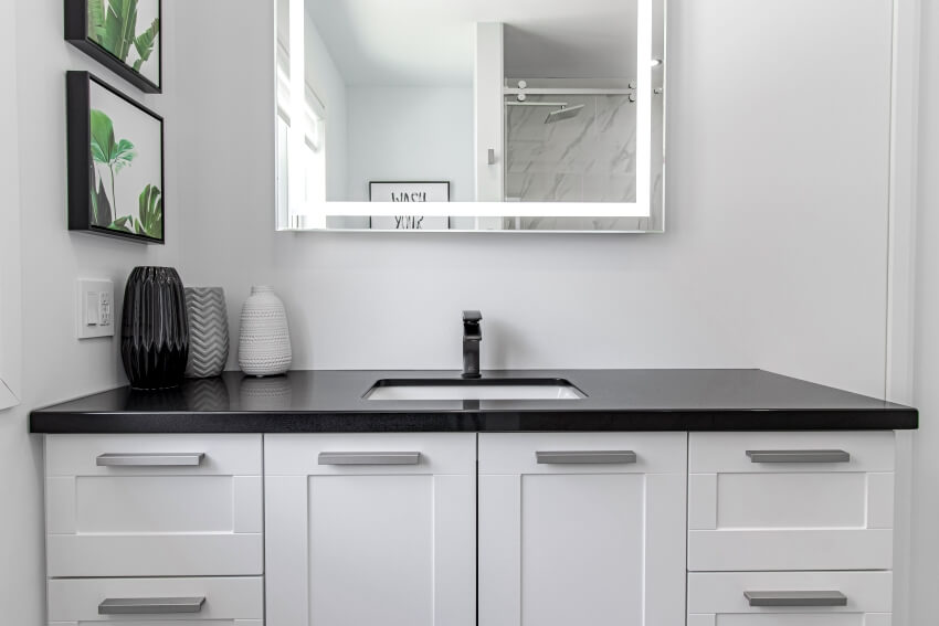 Bathroom interior with black laminate bathroom countertop with vase on top, white cabinets and a vanity mirror