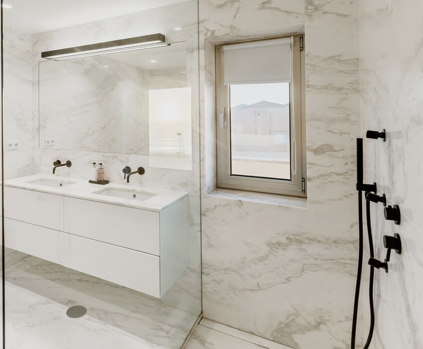 Bookmatched marble bathroom interior design with glass shower wall and white sink