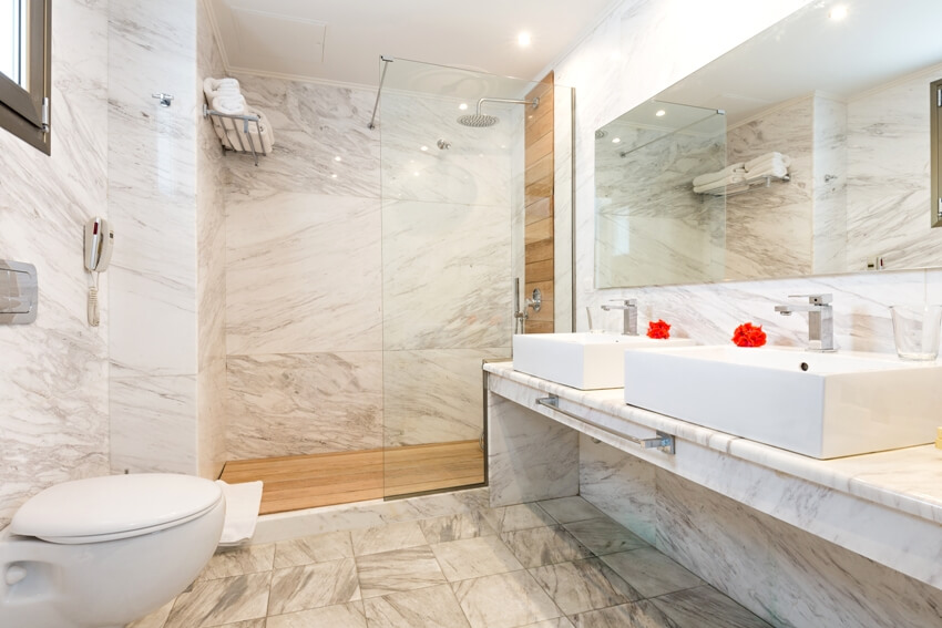 A bookmatched marble bathroom interior with glass shower wall, sinks on countertop, and a toilet