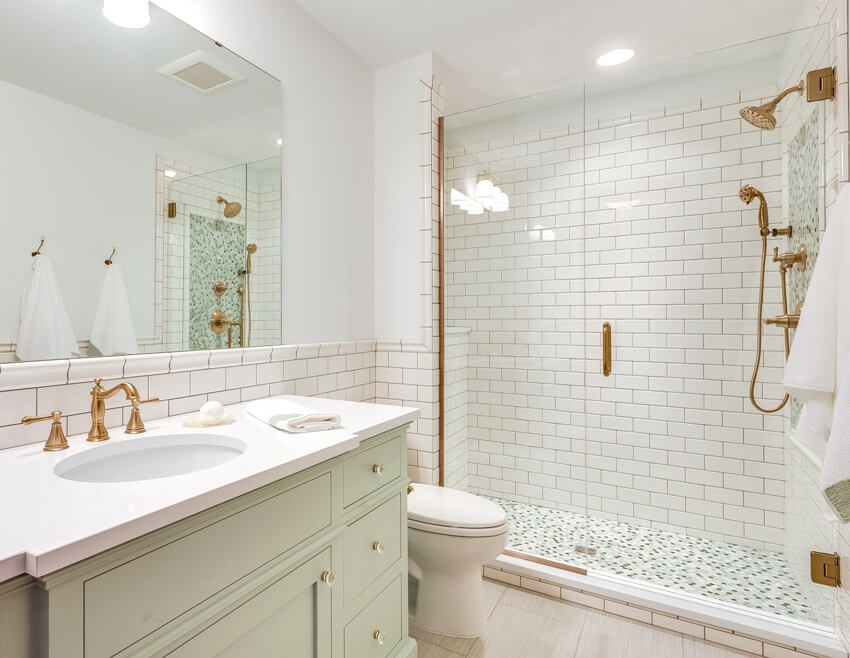 Bright bathroom with shades of green, penny tile floors and brass fixtures in shower