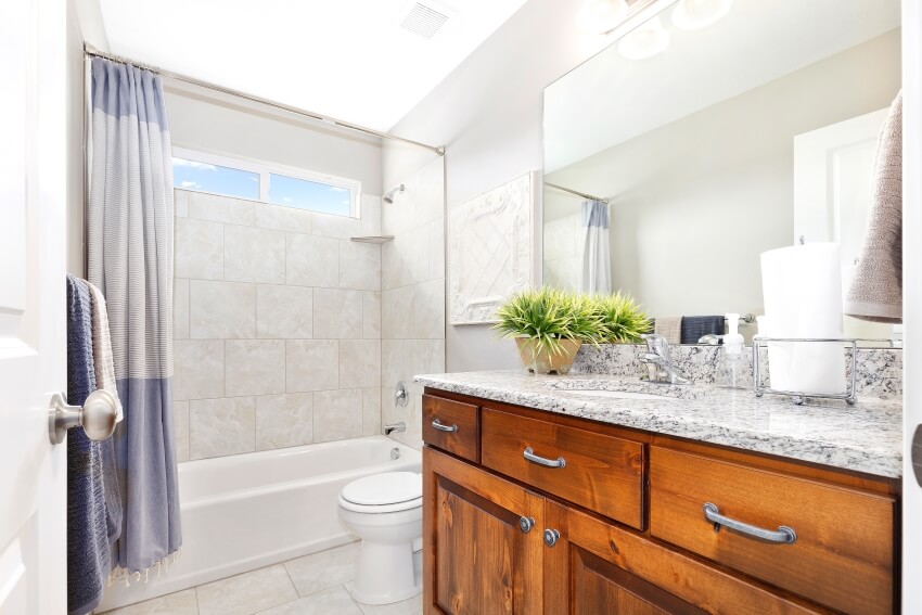 Bright bathroom with wooden cabinet and granite top vanity, tile walls, and shower curtain