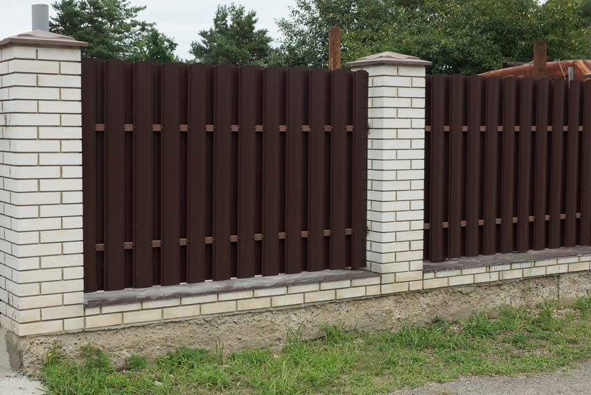 Brown shadowbox fence made of metal and supported by white brick pillars