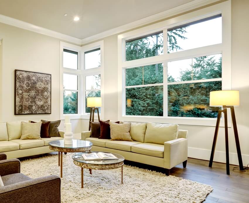 Chic light living room design with security window film tints furnished with glass top accent tables and beige sofas topped with brown pillows