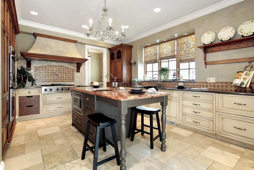 French country kitchen with distressed white cabinets, chandelier, and travertine floors