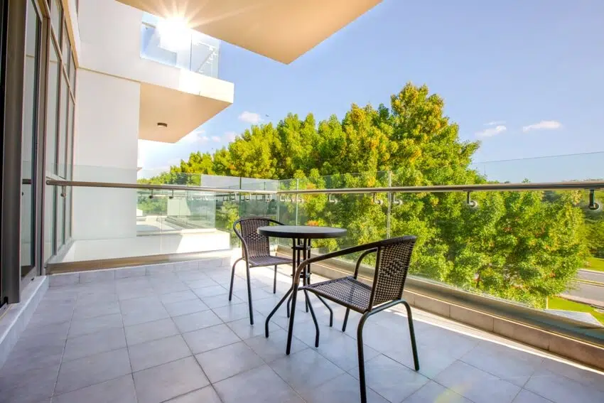 Coffee table and chairs in a balcony with glass railings and lush green trees view