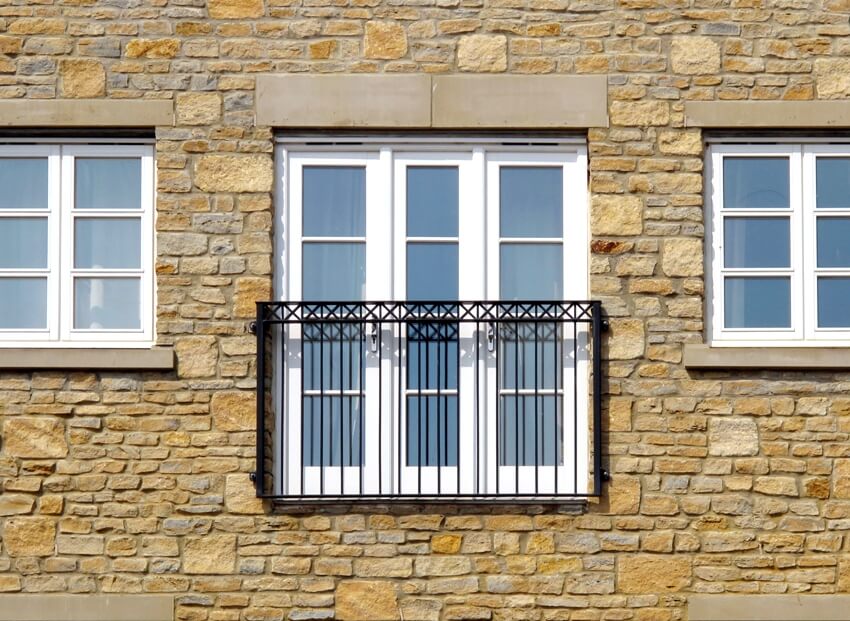 A contemporary juliet balcony and three windows in apartment with stone exterior