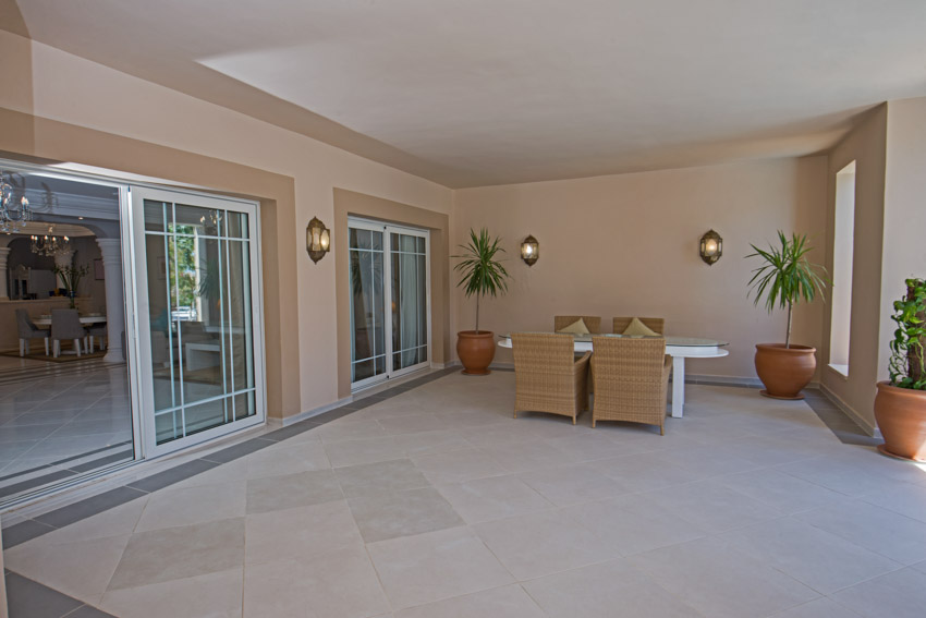 Covered patio with sliding glass door, wall mounted lights, table, chairs, and potted plants