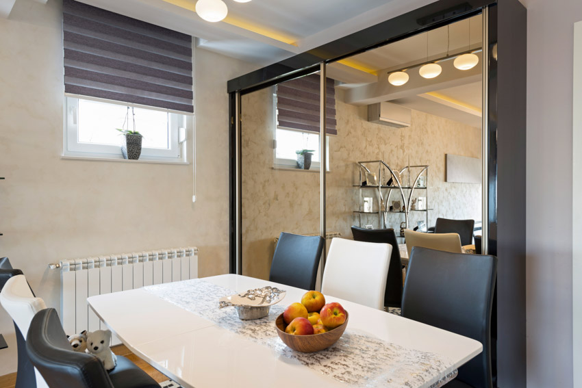 Dining room with mirror wall panel, table, chairs, and window blinds