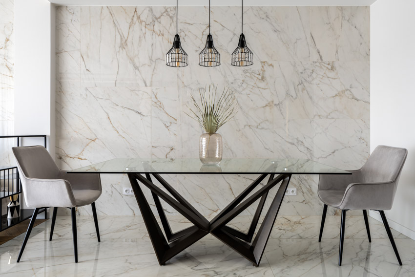 Dining room with modern table, glass top, chairs, marble accent wall, and hanging lights