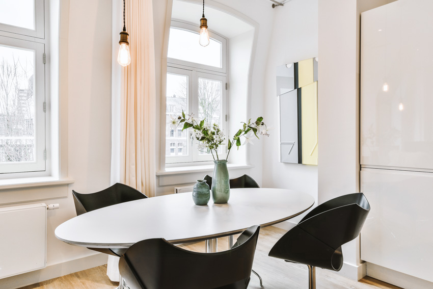 Dining room with oval shaped table, black chairs, hanging lights, and windows