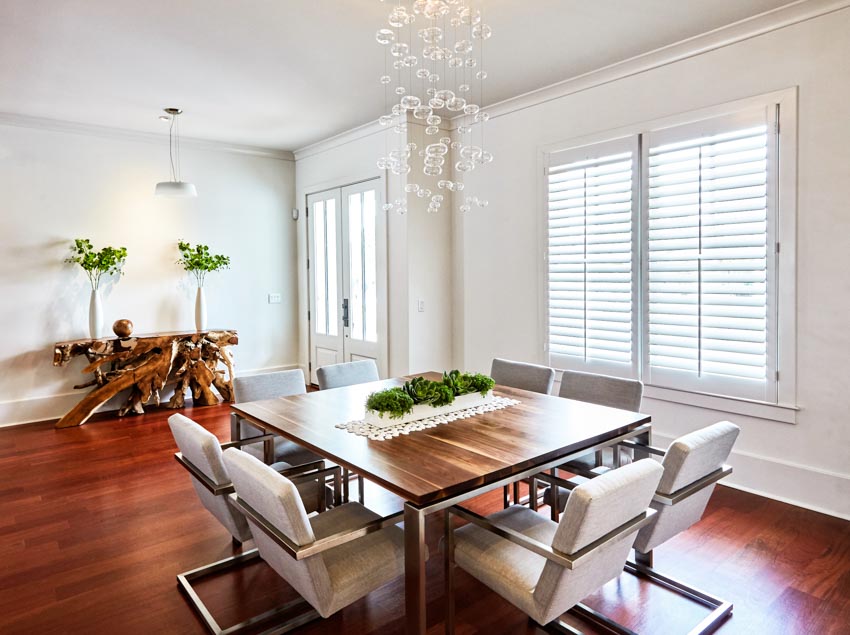 Dining room with plantation shutters, wood floor, dining table, chairs, chandelier, and indoor plants