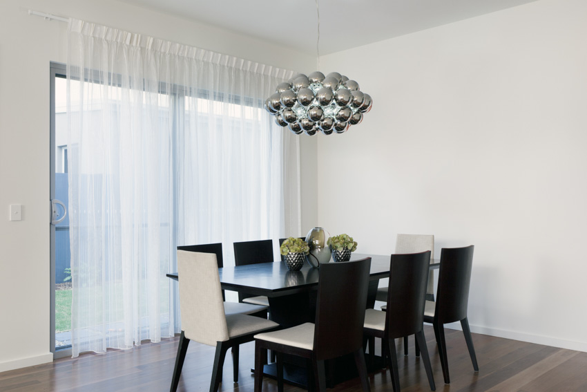 Dining room with table, chairs, hanging light, wooden floors, and window curtains