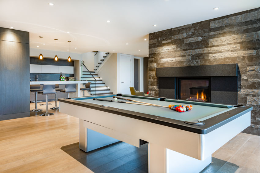Entertainment room with pool table, bar area, hanging light, fireplace, and wood floors