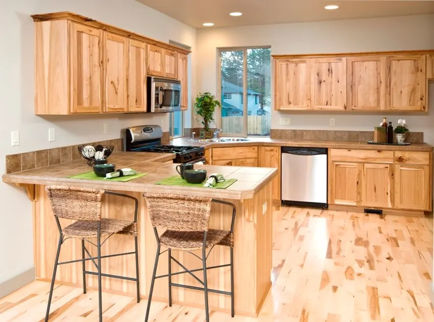 A fresh looking kitchen interior with tiled countertops, knotty pine kitchen cabinets, and flooring