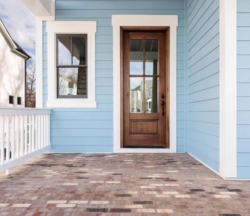 Front porch with blue siding, brown front door, and egress window