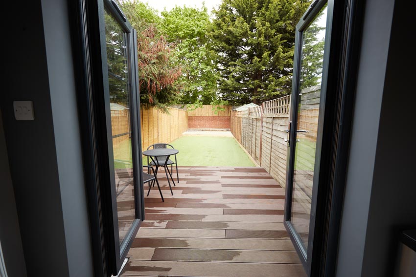 Glass patio door leading to outdoor area with wood deck, table, chairs, and wooden fence