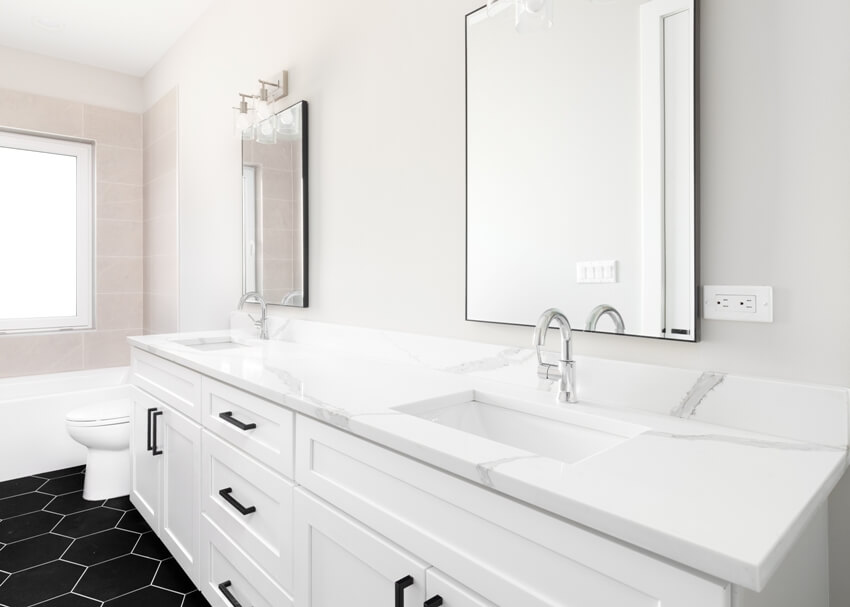 Gorgeous bathroom with white vanity cabinets and laminate marble countertop, black hexagon tiled floor and a brown tiled shower
