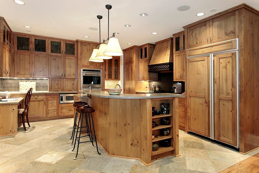 Gorgeous kitchen with unfinished knotty wood grain cabinets, marble floors, and integrated appliances