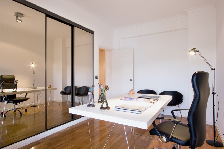 Office area with mirror, black chair, white desk with lamp