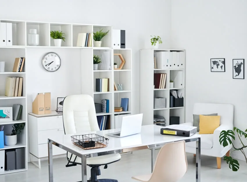 Home office with desk, armchair, open shelf filing cabinets, green plant and two pictures on wall