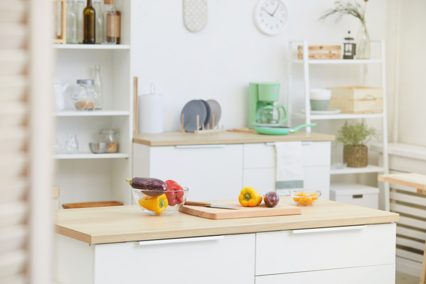 House interior with kitchen table, wood countertop, cutting board, shelves, and white wall