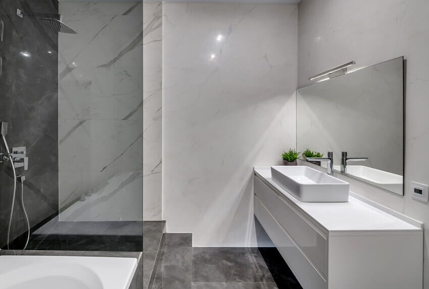 Interior of a modern bathroom with marble walls, laminate countertop and gray tiled floors