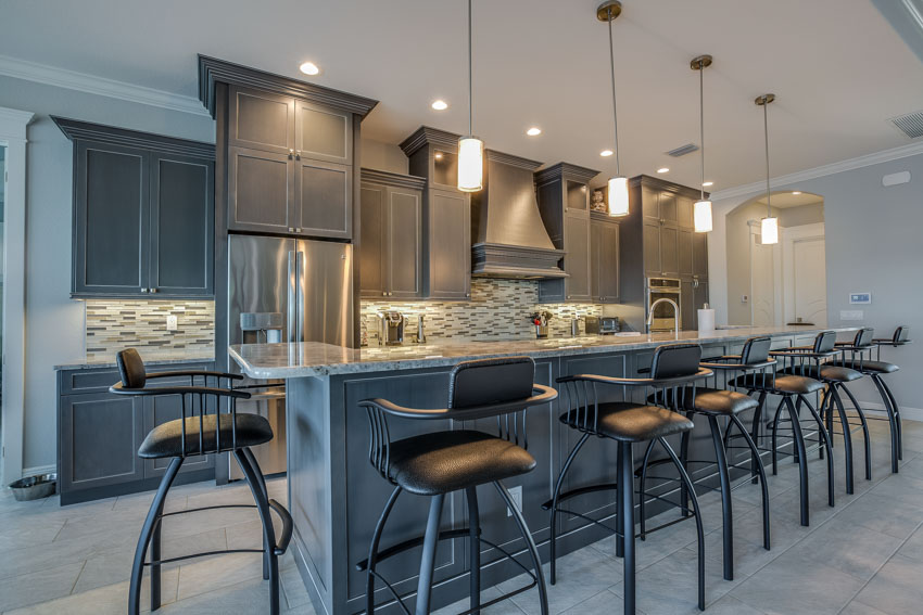 Kitchen with a long island, cushioned bar stools, pendant lights, backsplash, and gray cabinets