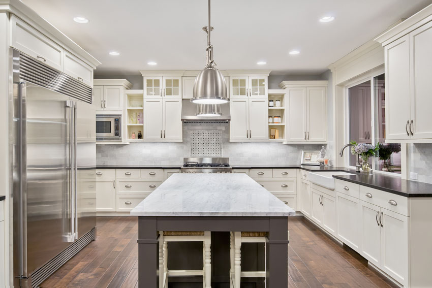 Kitchen with Carrara marble backsplash, countertop, island, wood flooring, cabinets, drawers, range hood, and pendant light