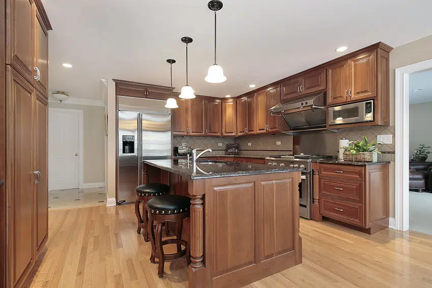 Kitchen with center island, wood flooring, pecan cabinets, range hood, stove, bar stools, and hanging lights