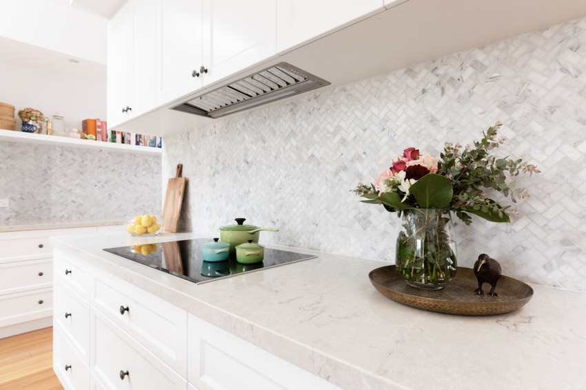 Kitchen with herringbone Carrara marble backsplash, countertop, induction, stove, and cabinets