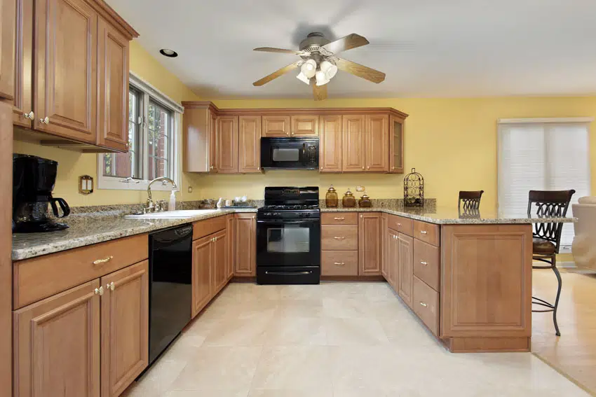 Kitchen with pecan wood cabinets, black oven, stove, countertop, ceiling fan, and yellow walls