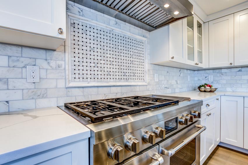 Kitchen with stove, oven, Carrara marble backsplash, and white cabinets