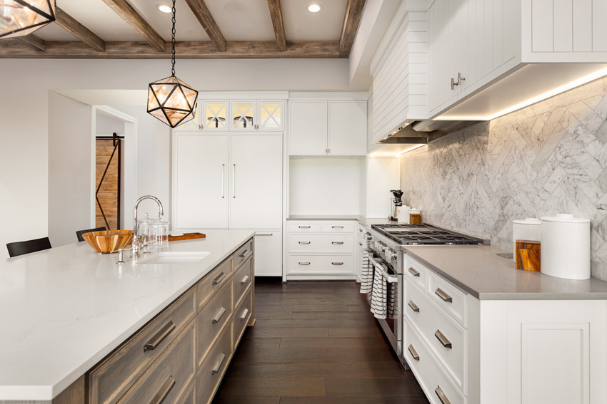 Kitchen with wood floor, Carrara marble backsplash, countertop, island, exposed ceiling beam, and white cabinets