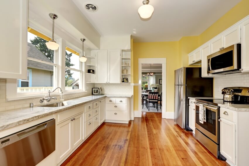 A large kitchen room with marble counter tops, wooden floors and vintage looking shaker cabinets