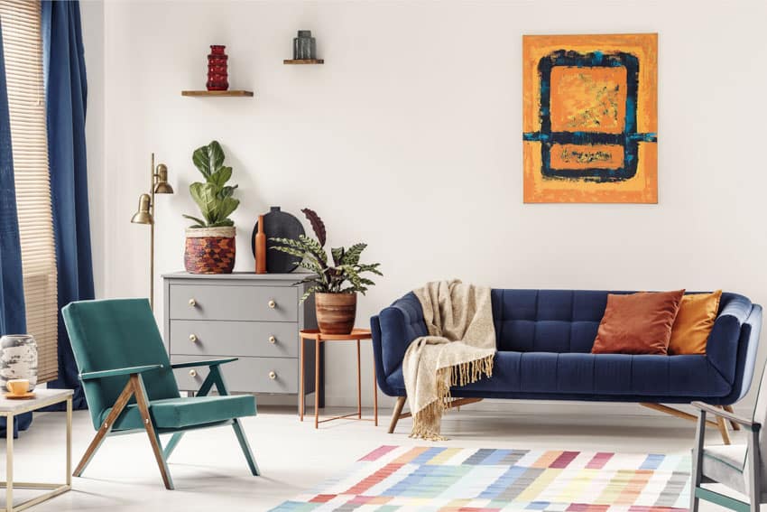 Living room with blue couch, sofa chair, floor rug, dresser, end table, and indoor plants